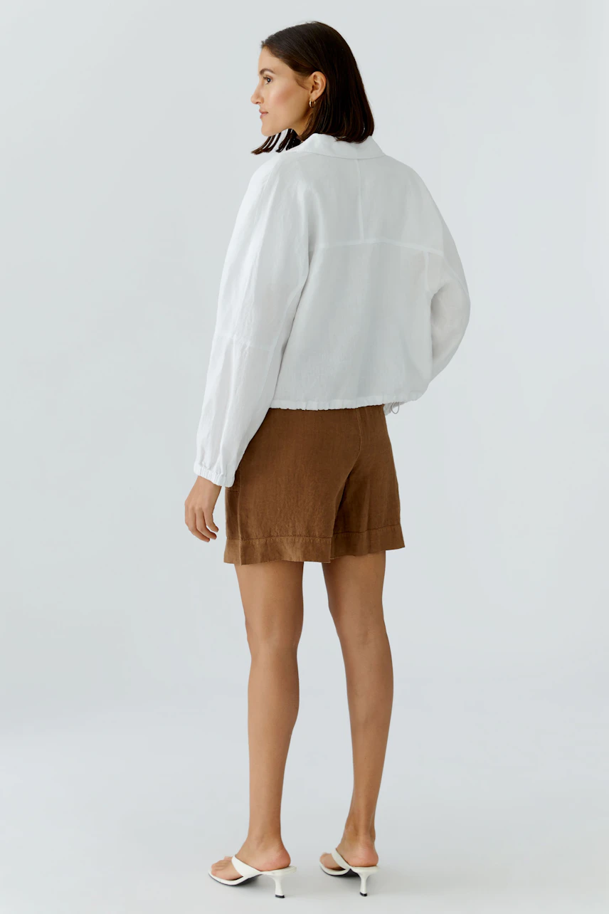 Lässiger Blouson: Frau in weißem Blouson und braunen Shorts, seitlich stehend, mit offenen Haaren.