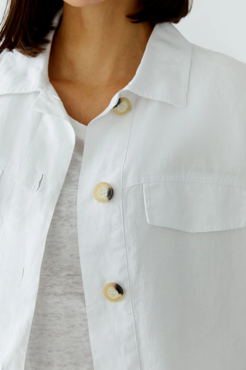 Damen-Blouson: Frau in weißem Blouson mit Knopfleiste und Brusttasche über grauem Shirt.