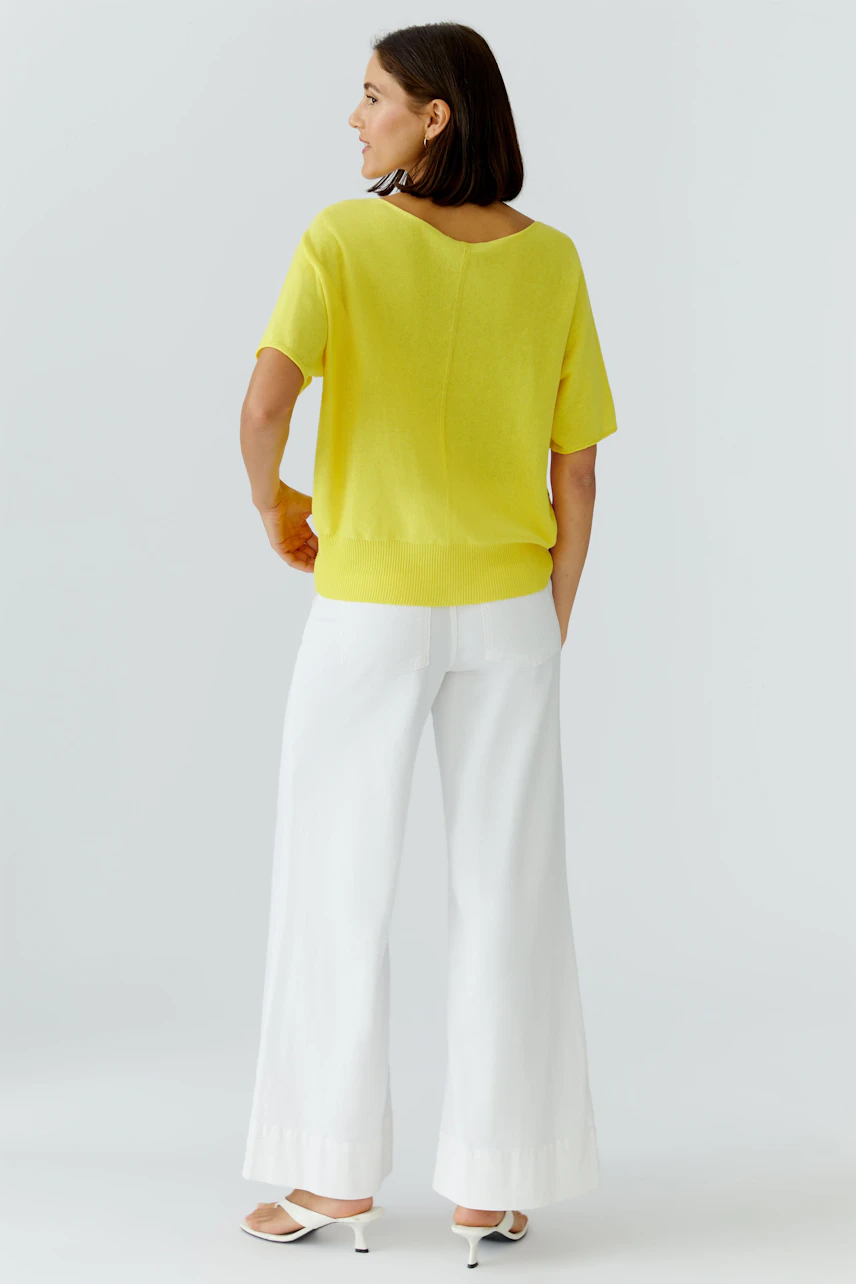 Casual women's pullover: Woman in a bright yellow pullover and white pants, viewed from the back.