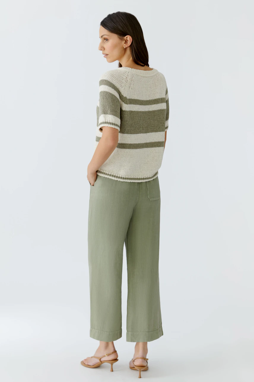 Casual women's pullover: Woman in striped pullover and green pants, standing sideways, looking relaxed.