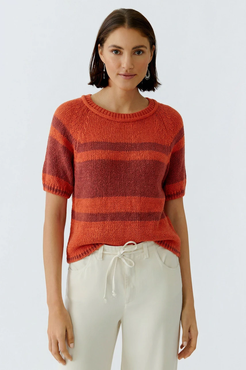 Frau im gestreiften Pullover in Rot-Orange, kombiniert mit heller Hose. Lässiger Look für den Alltag.