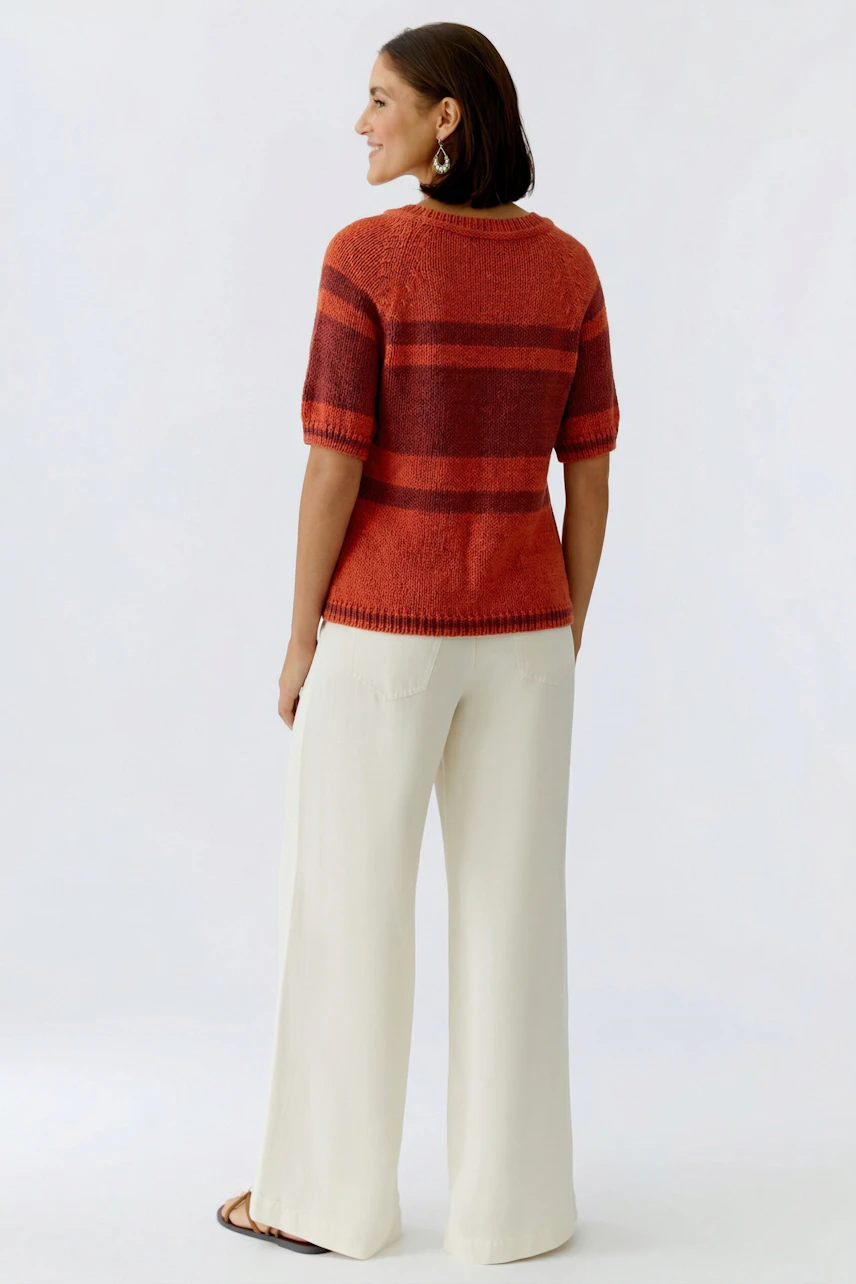 Casual women's pullover: A woman in a striped pullover with orange and gray tones, paired with wide jeans.