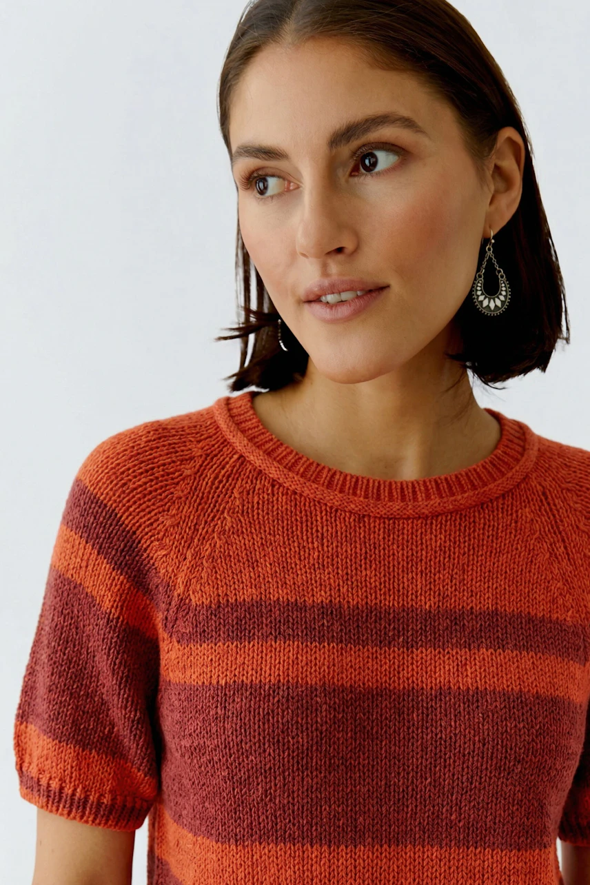 Frau im gestreiften Pullover in Rot- und Orangetönen, lässig und modern, mit kurzen Ärmeln.