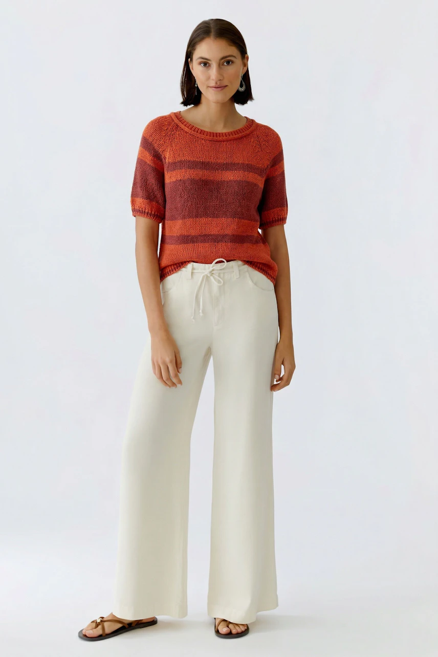Casual women's pullover: A woman in a striped pullover with orange and gray tones, paired with wide jeans.