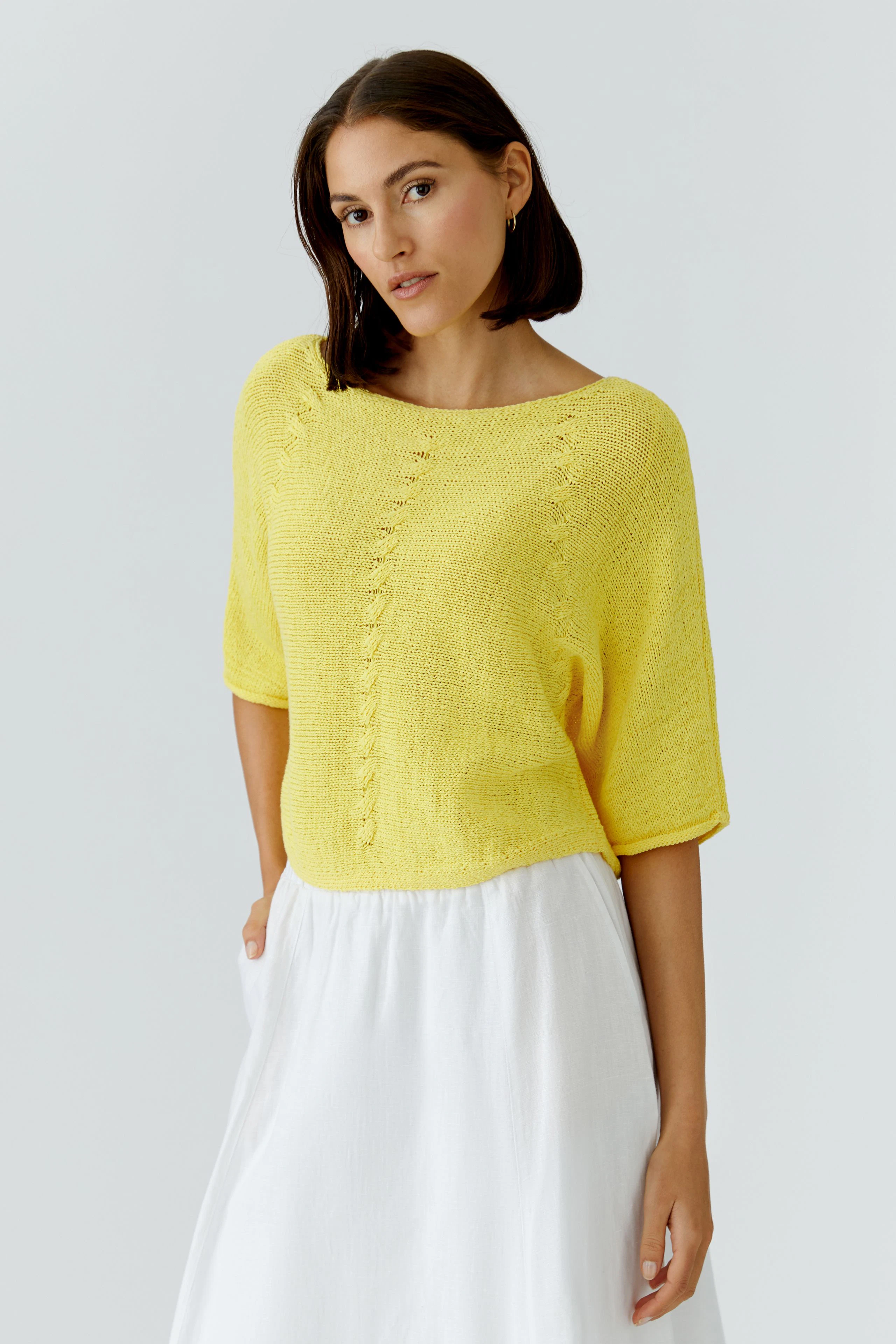 Casual women's pullover: Woman in a bright yellow pullover with a relaxed fit, paired with a white skirt.