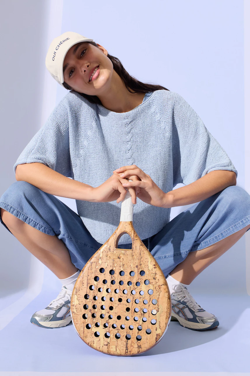 Casual women's pullover: Woman in light blue pullover, denim pants, and sneakers, holding a paddle.