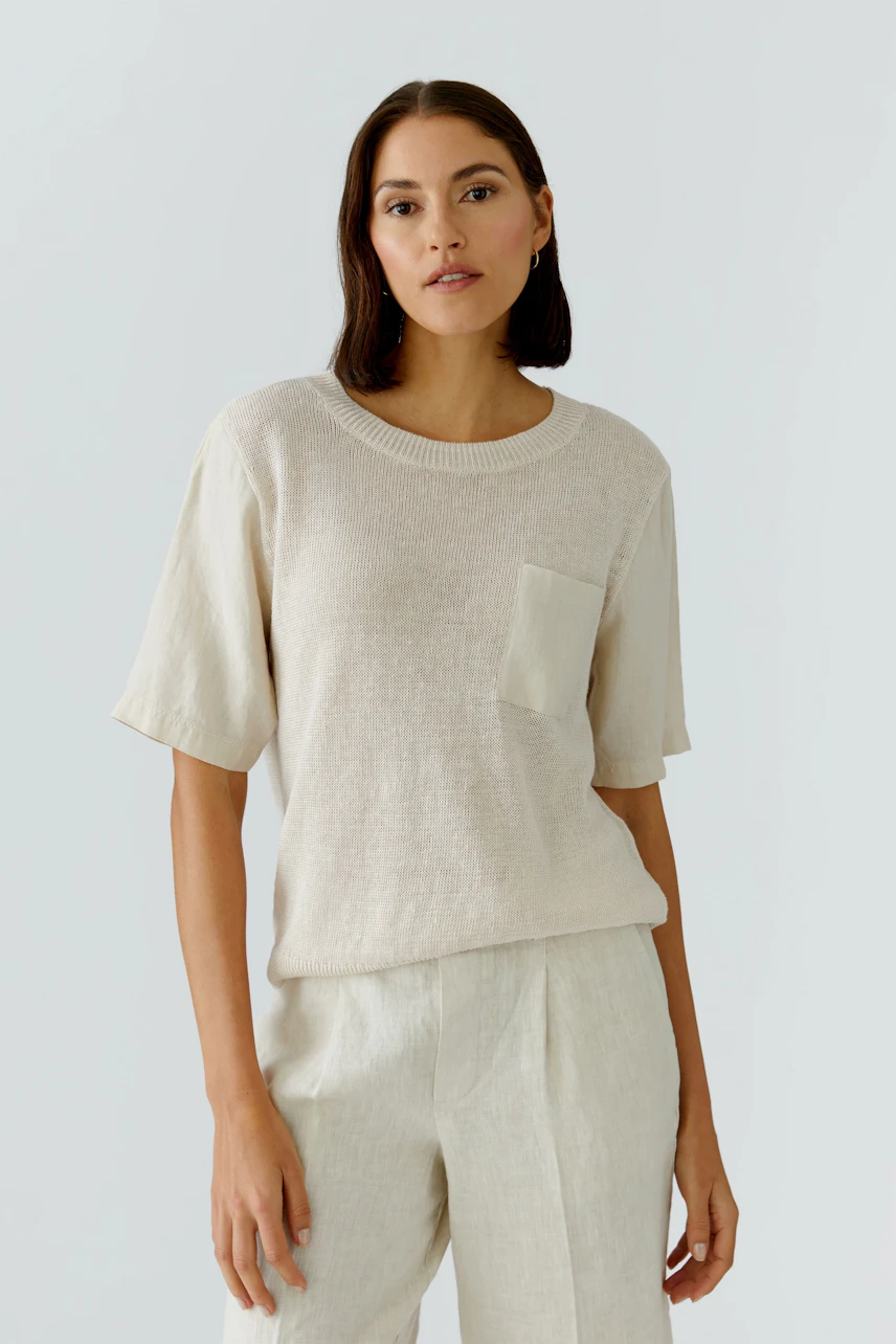 Damen-Pullover: Frau im beigen Pullover mit Brusttasche und kurzen Ärmeln, kombiniert mit heller Hose.