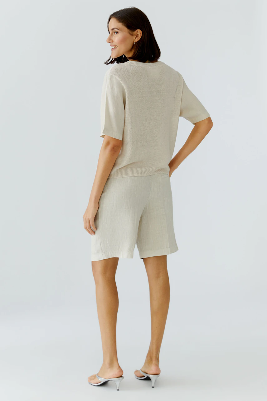 Lässiger Damen-Pullover: Frau in hellem Pullover und Shorts, seitlich stehend, mit entspanntem Ausdruck.