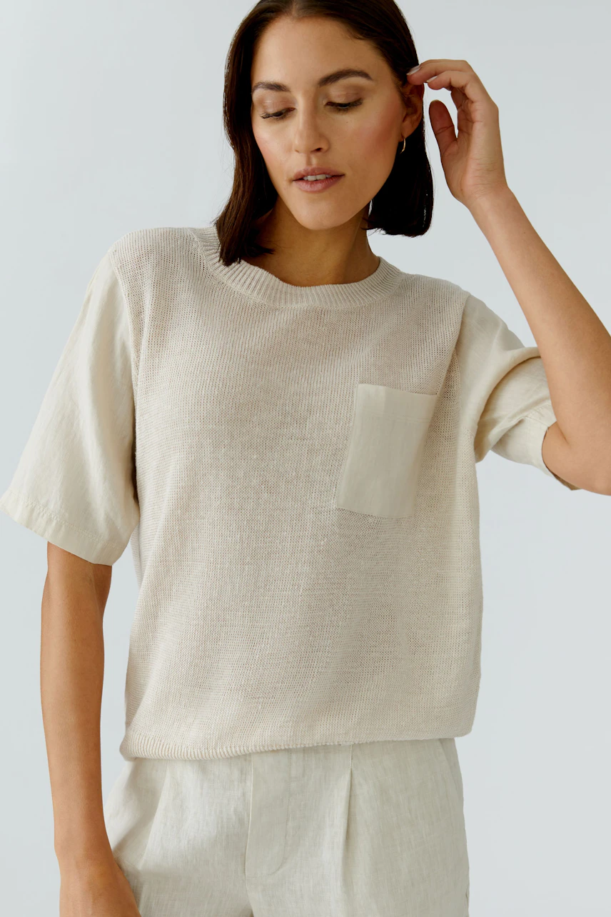 Damen-Pullover: Frau im beigen Pullover mit Brusttasche, kombiniert mit heller Hose, wirkt entspannt.