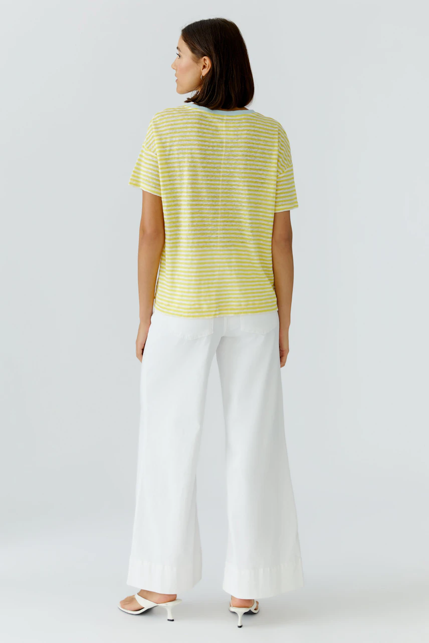 Gestreiftes Damen-T-Shirt: Frau im gelb-weiß gestreiften T-Shirt und weißen Hosen, von hinten gesehen.