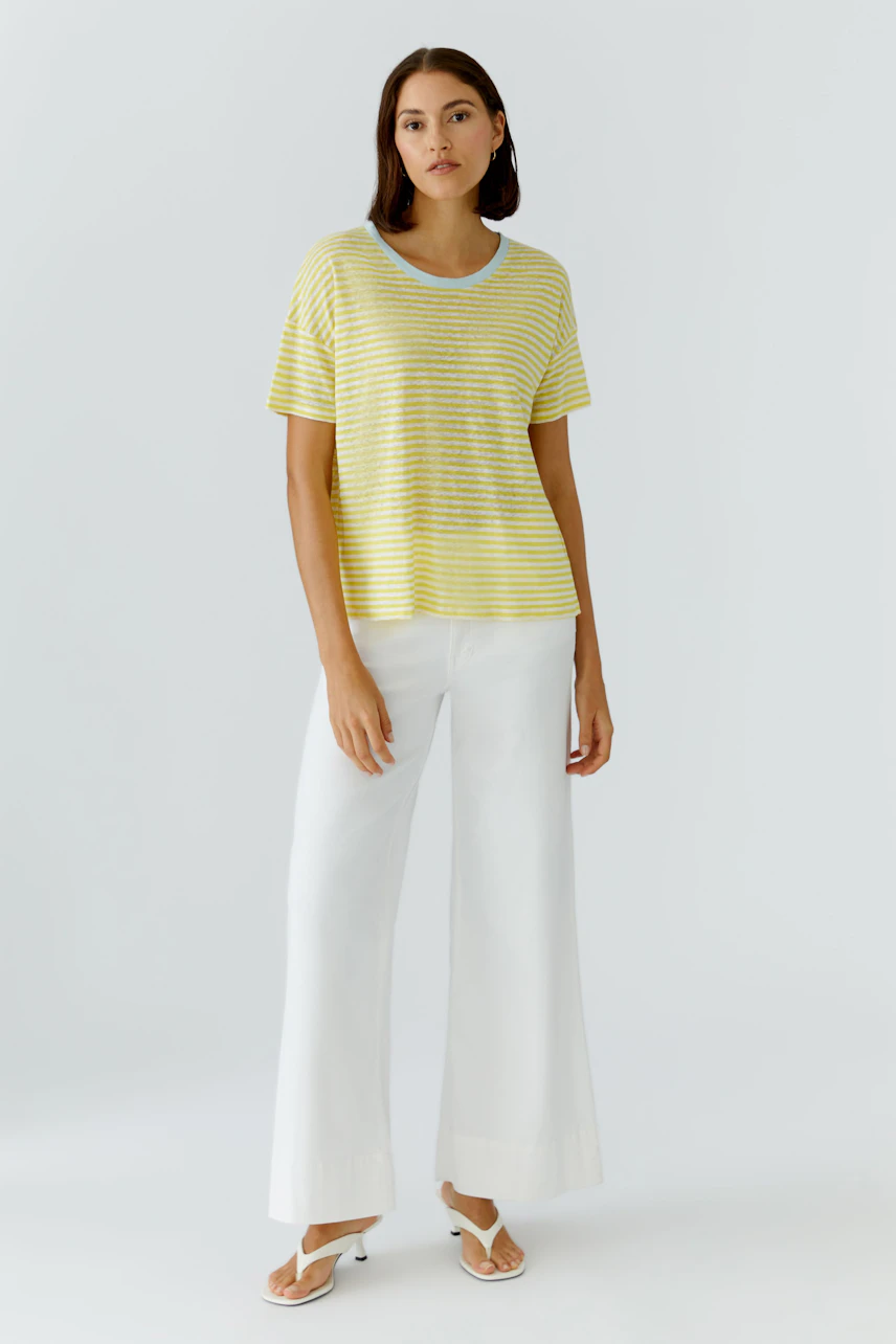 Lässiges Damen-T-Shirt: Frau im gelb-weiß gestreiften T-Shirt und weißen Hosen steht entspannt.