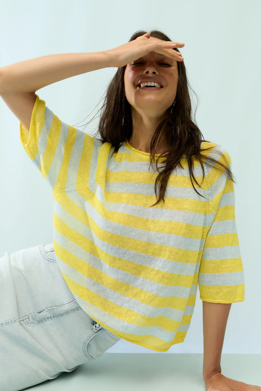 Casual women's pullover: Woman in yellow striped pullover, relaxed and smiling.