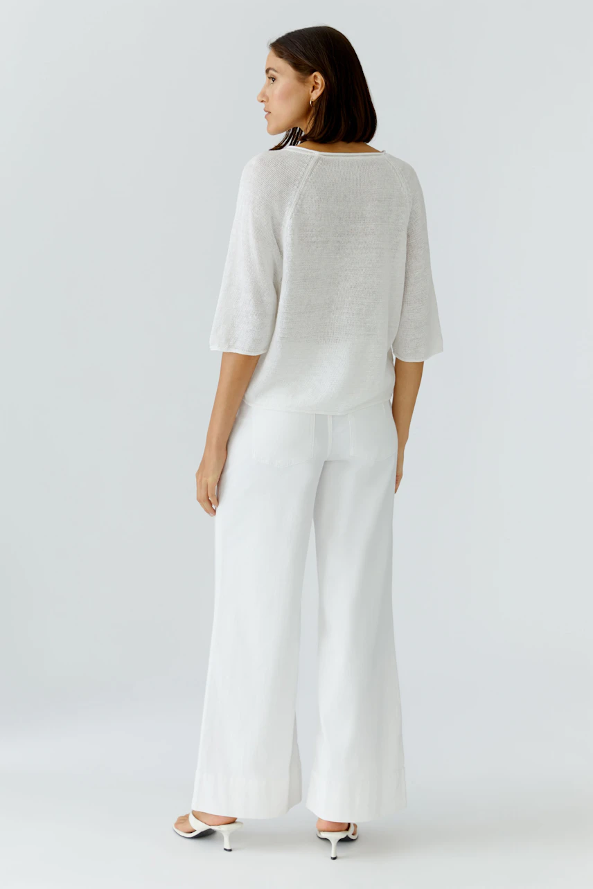 Lässiger Damen-Pullover: Frau im weißen Pullover und weiter Hose, von hinten gesehen.