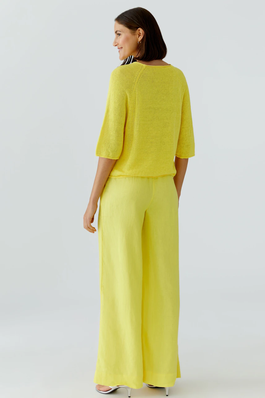 Frau im gelben Pullover und passender Hose, lässig und modern, von hinten gesehen.