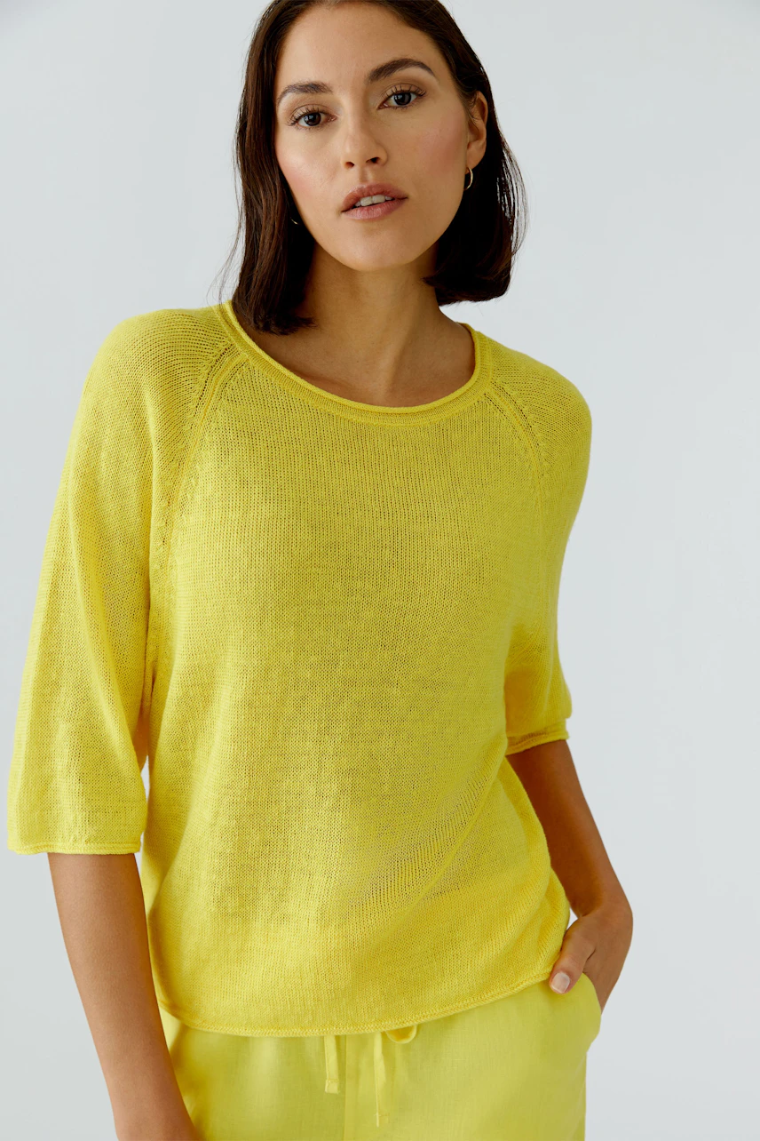 Frau im gelben Pullover mit Dreiviertelärmeln, lässig und modern, blickt direkt in die Kamera.