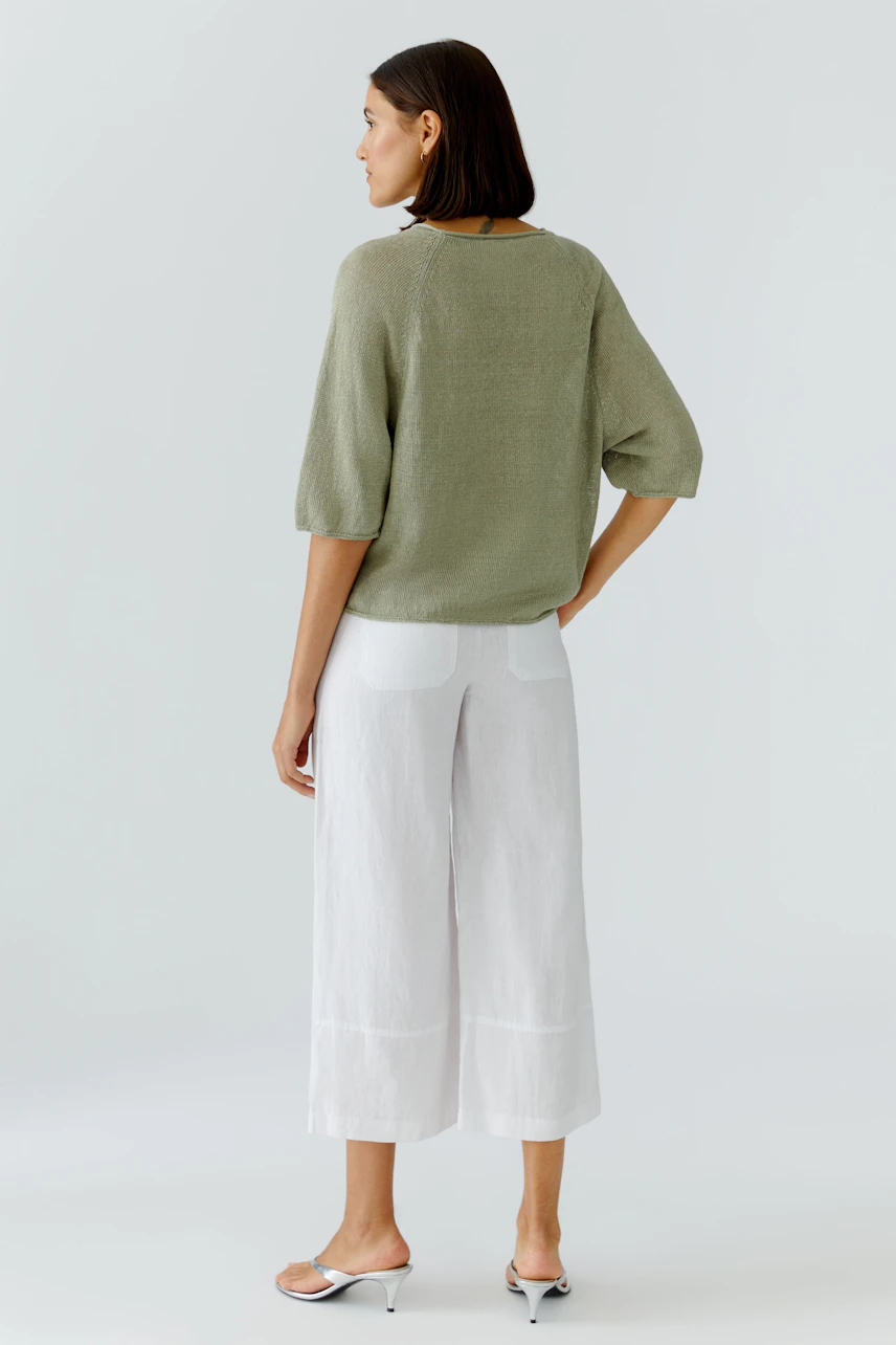 Damen-Pullover: Frau im lockeren, olivgrünen Pullover und weißen Hosen, von hinten gesehen.