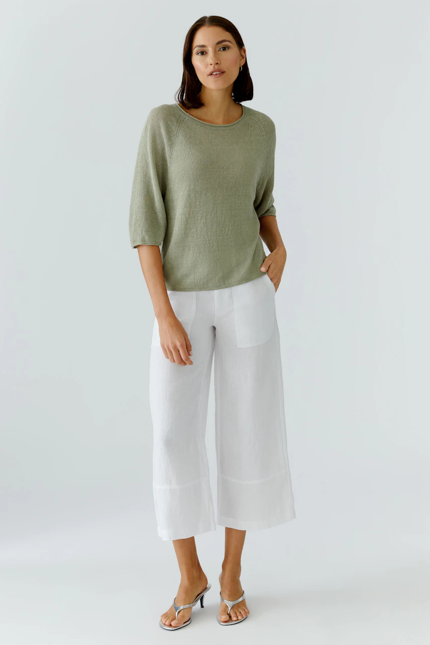 Lässiger Damen-Pullover: Frau im grünen Pullover und weißen Hosen, entspannt und stilvoll.