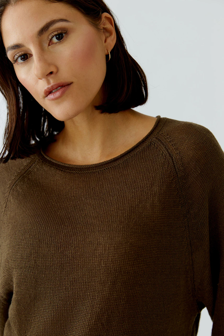 Frau im braunen Pullover mit Rundhalsausschnitt, lässiger Look, dezente Ohrringe.