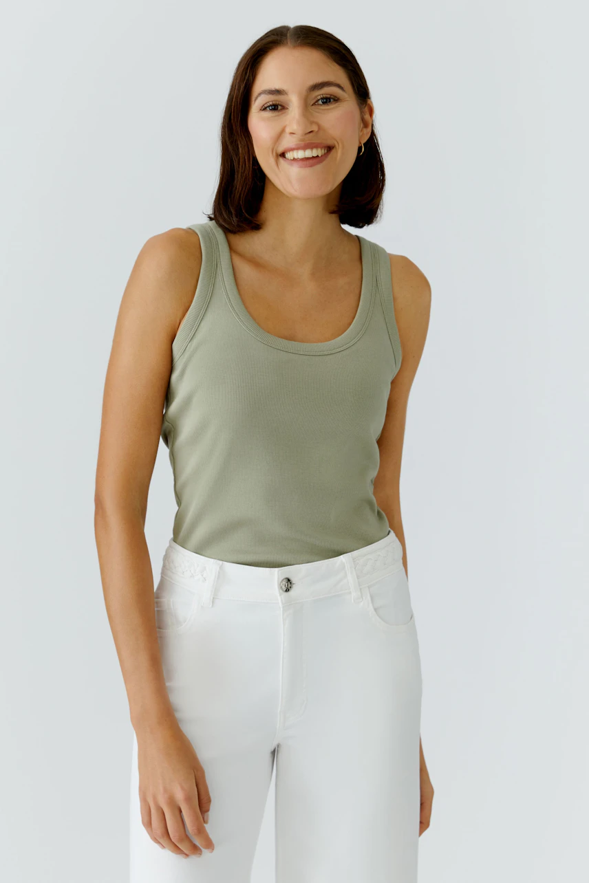 Casual tank top: Smiling woman in a green tank top and white pants, exuding a relaxed vibe.