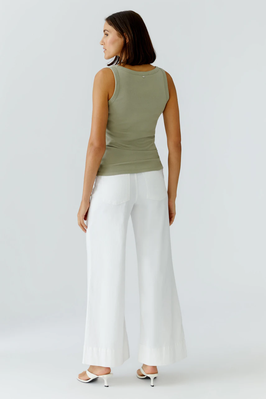 Casual tank top: Woman in olive green tank top and white wide-leg pants, standing confidently.
