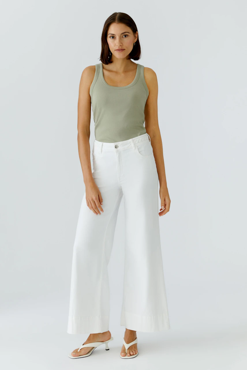 Casual tank top: Woman in a green tank top with white wide-leg pants and sandals, standing confidently.