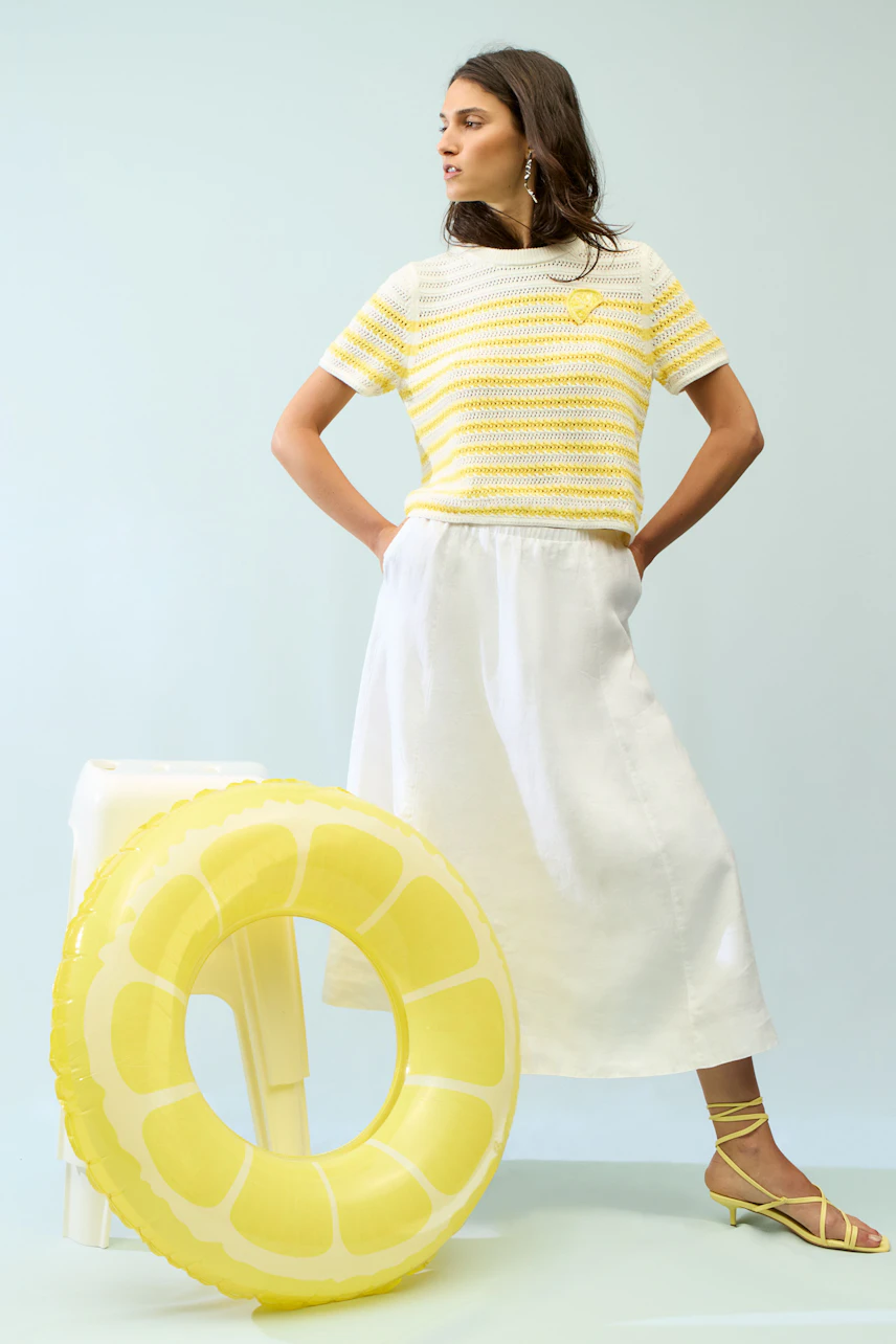 A-line skirt: Woman in a white A-line skirt with a yellow striped top, standing confidently.