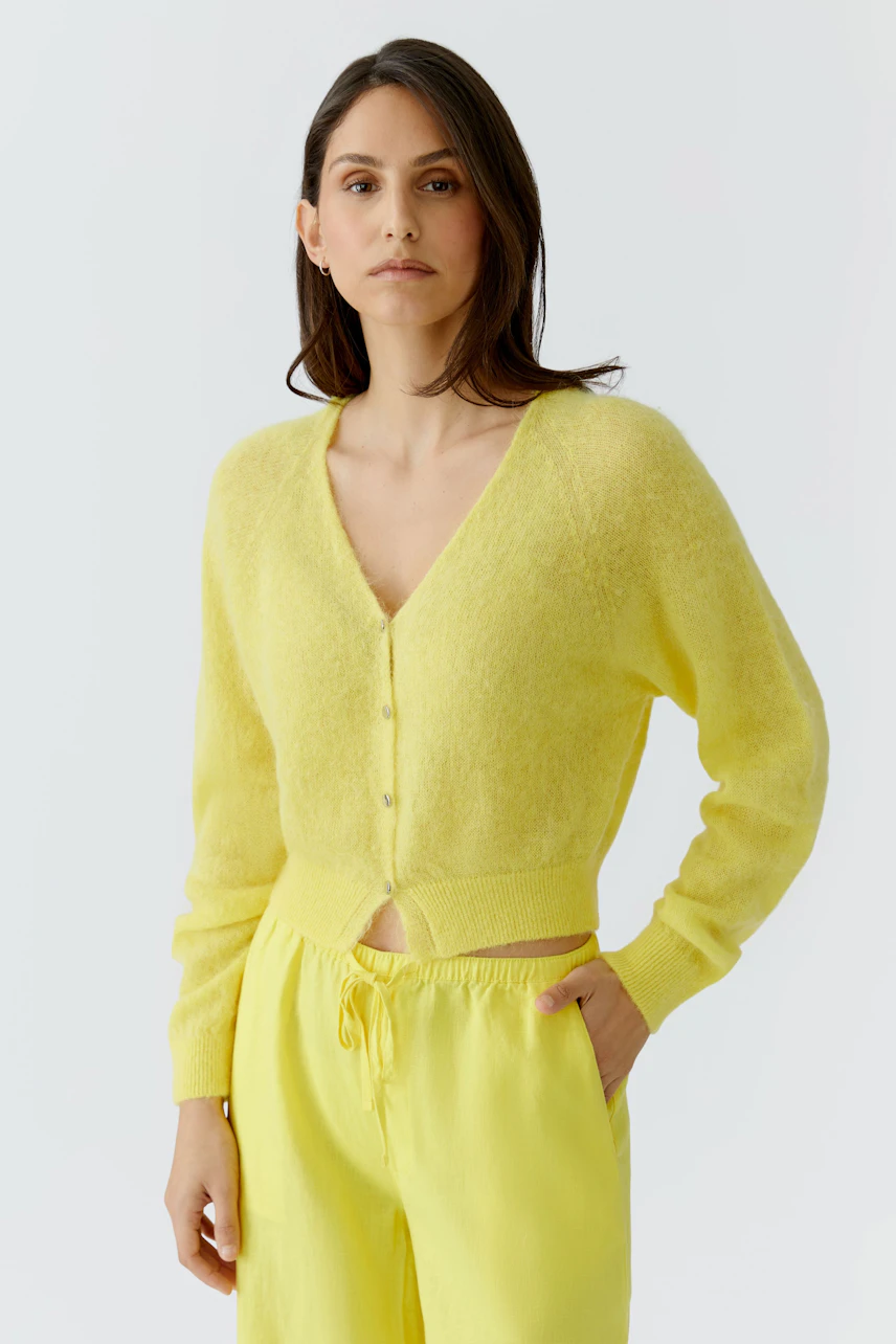 Woman in a yellow cardigan and matching pants, looking confidently. Casual and stylish knitwear.
