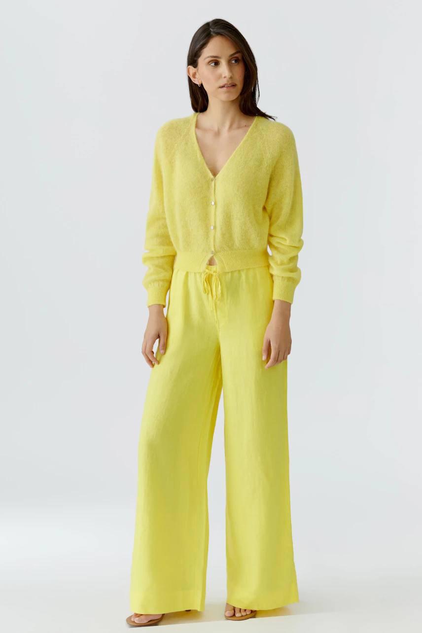 Woman in a yellow cardigan and matching wide-leg pants, standing confidently.