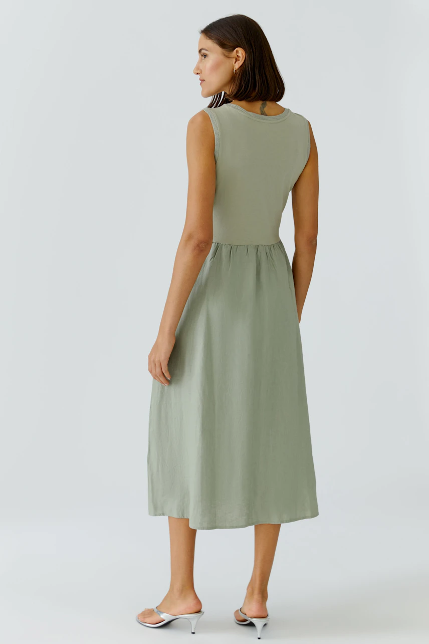 Casual midi dress: Woman in sleeveless green dress, standing with relaxed posture, showcasing back view.