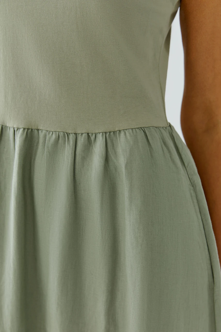 Casual midi dress: Woman in a sleeveless, light green dress with a gathered waist, standing confidently.