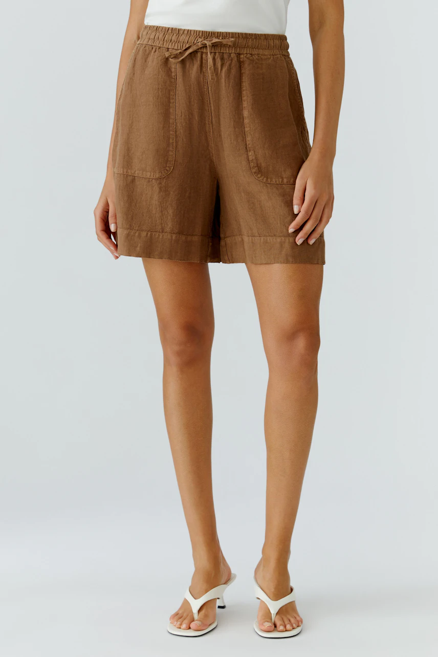 Casual women's shorts: Woman in brown shorts with drawstring waist and pockets, paired with white sandals.