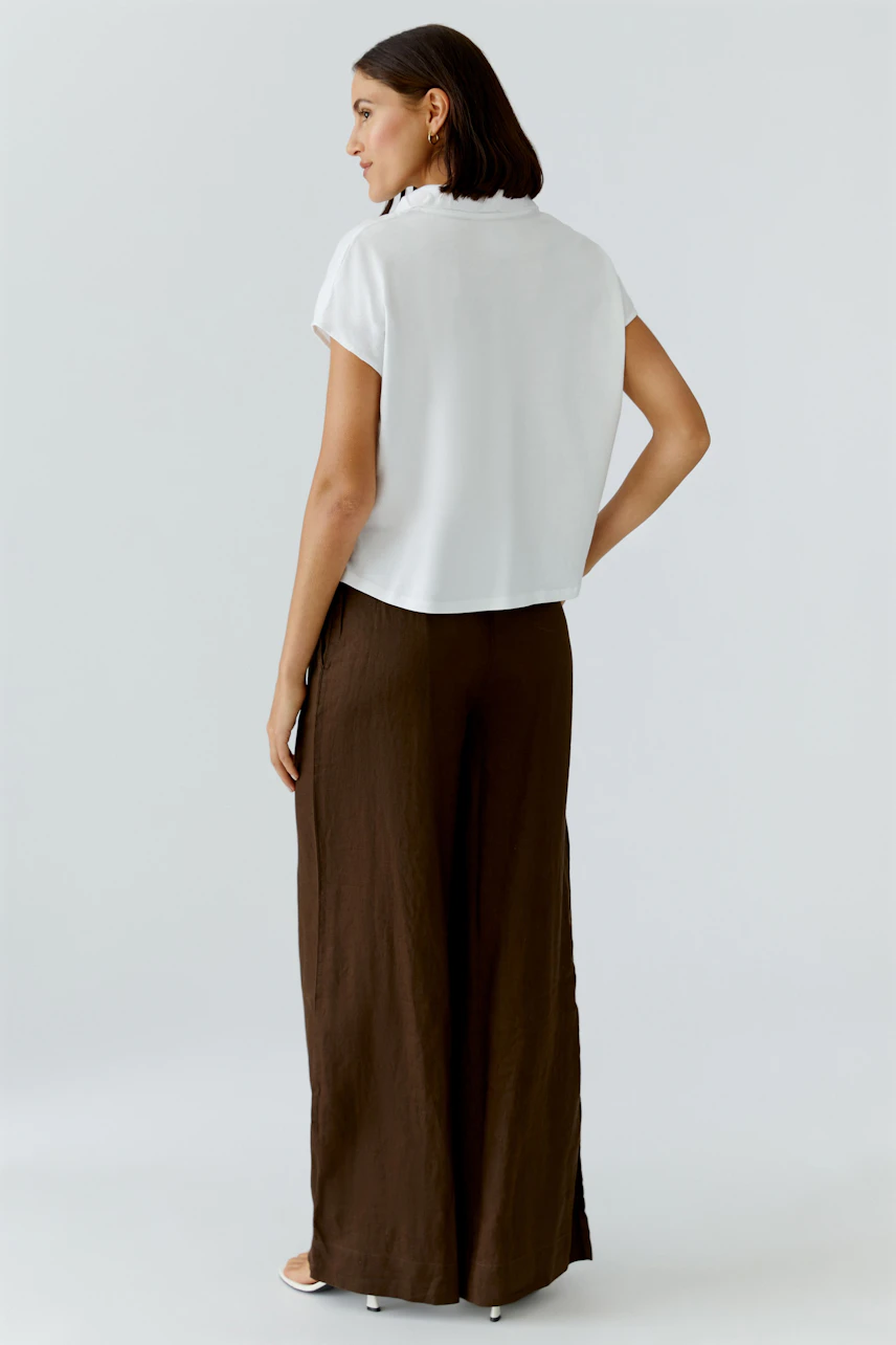 Casual women's blouse: Woman in a white blouse with short sleeves and brown wide-leg pants, standing confidently.
