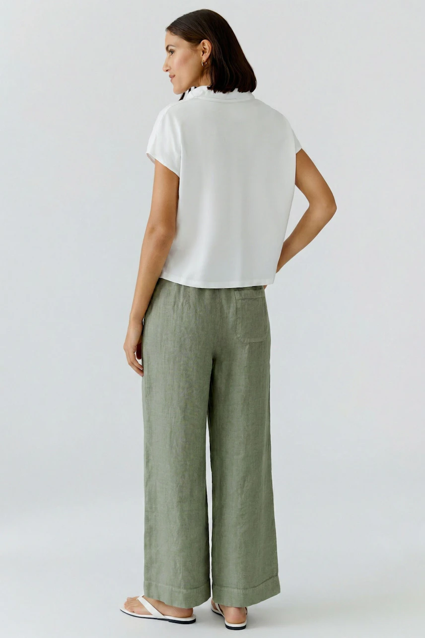 Casual women's blouse: Woman in a white blouse with short sleeves and brown wide-leg pants, standing confidently.