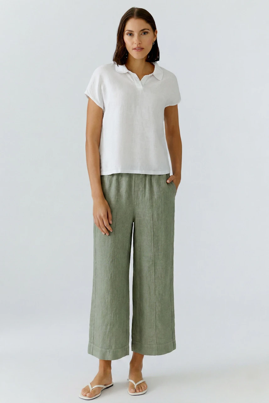 Casual blouse: Woman in a white blouse with short sleeves and brown wide-leg pants, standing confidently.