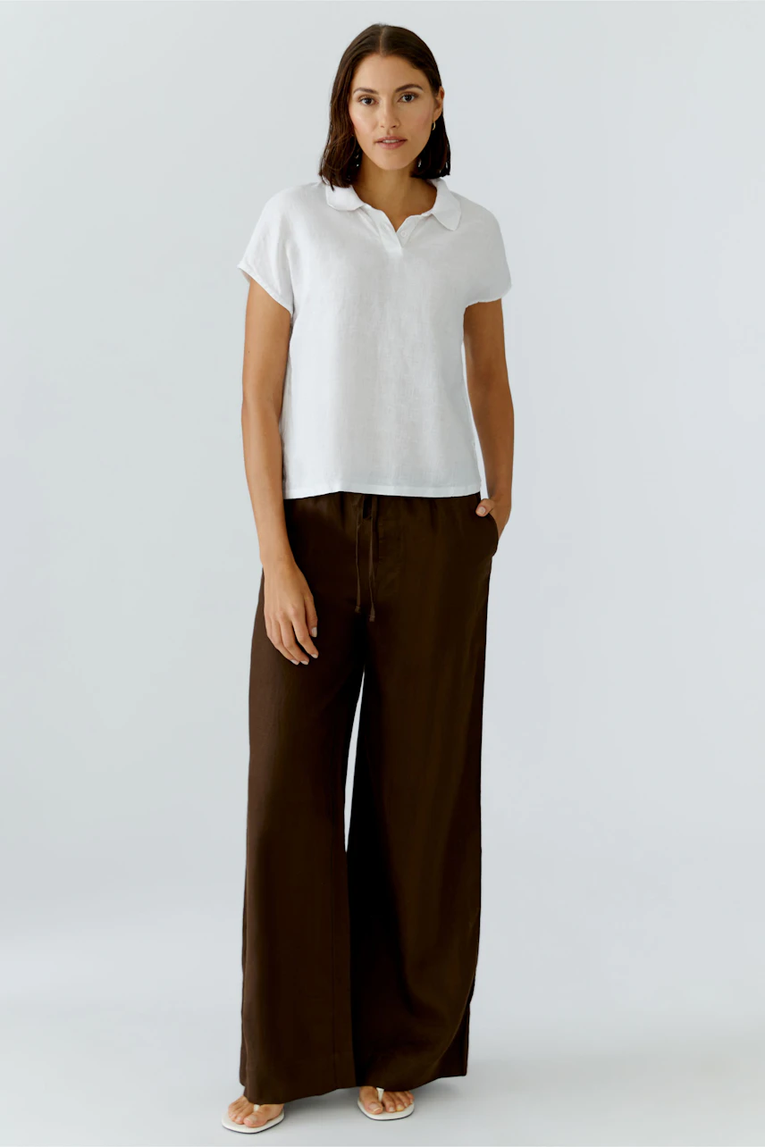 Casual blouse: Woman in a white blouse with short sleeves and brown wide-leg pants, standing confidently.