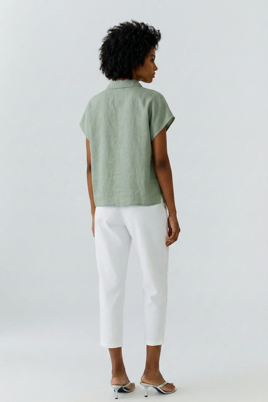 Casual blouse: Woman in a green short-sleeve blouse and white pants, standing confidently.