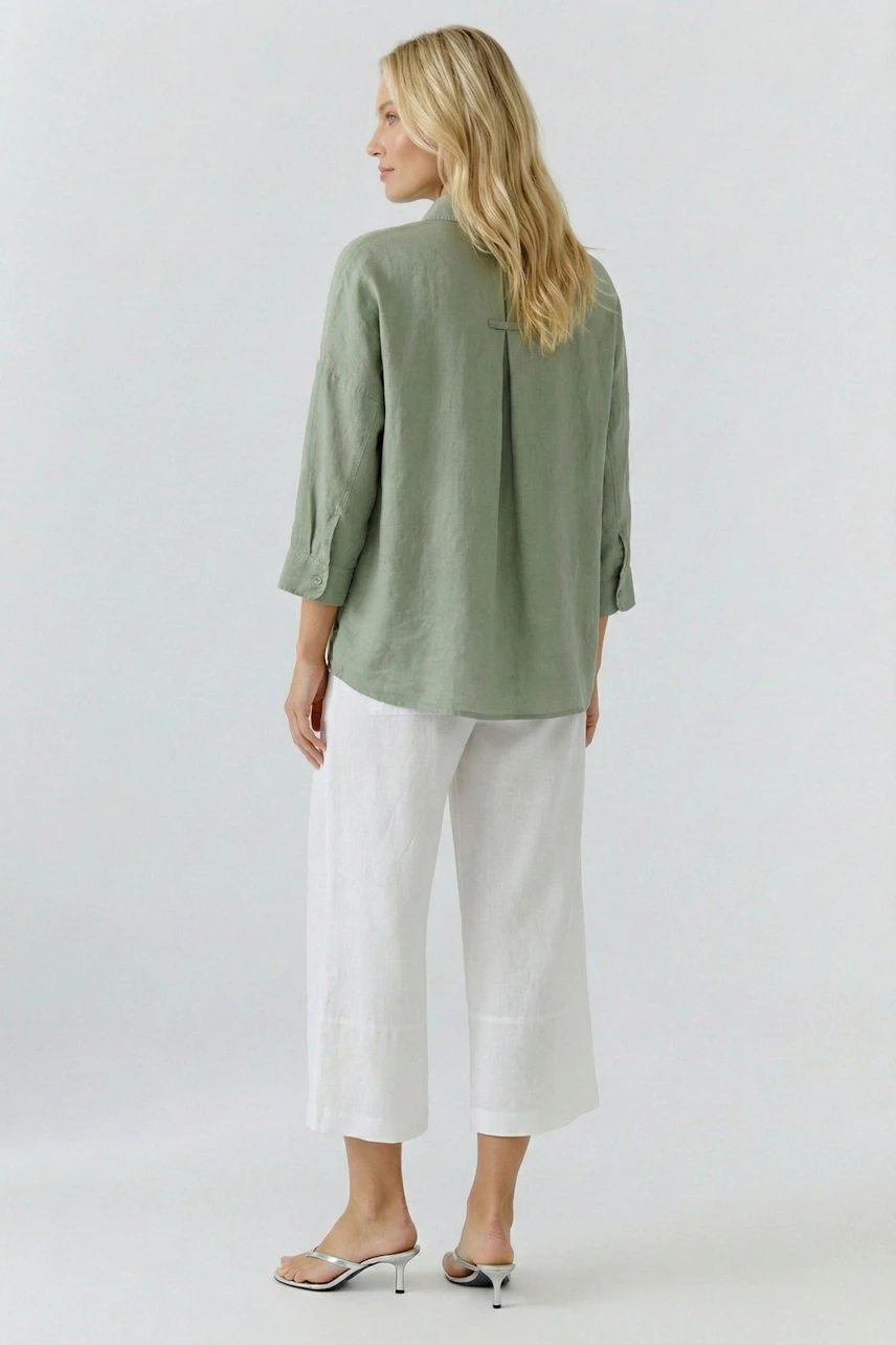 Casual blouse: Woman in a green blouse with rolled sleeves, paired with white pants, facing away.