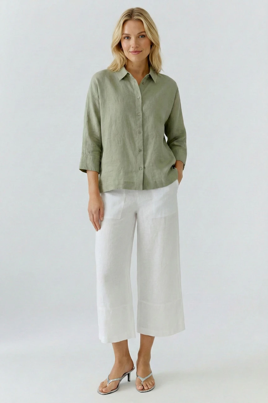 Casual blouse: Woman in a green button-up blouse with white wide-leg pants and sandals, standing confidently.