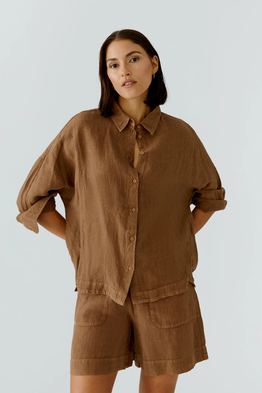 Casual women's blouse: Woman in a brown button-up blouse with rolled sleeves, paired with matching shorts.