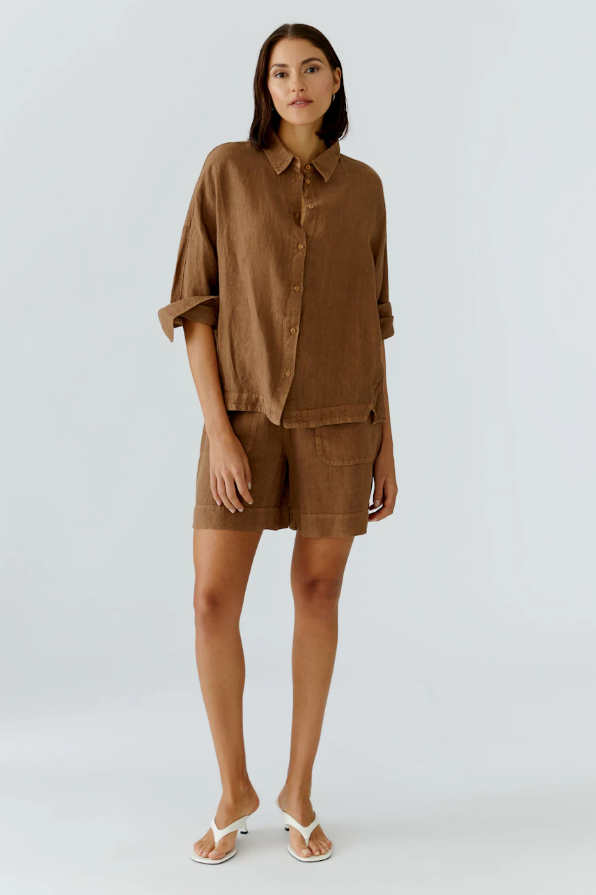 Casual women's blouse: Woman in a relaxed brown blouse with matching shorts and white sandals.