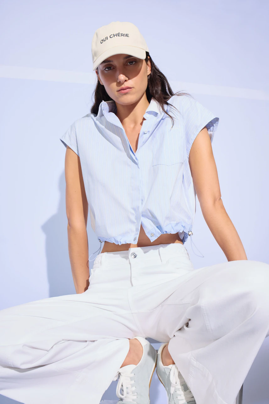 Casual blouse: Woman in a light blue blouse with cap sleeves, paired with white pants and a beige cap.