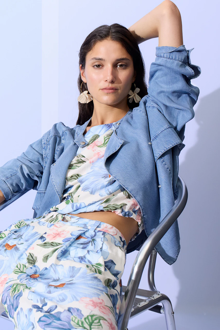 Floral blouse: Woman in a floral blouse and denim jacket, sitting confidently on a chair.