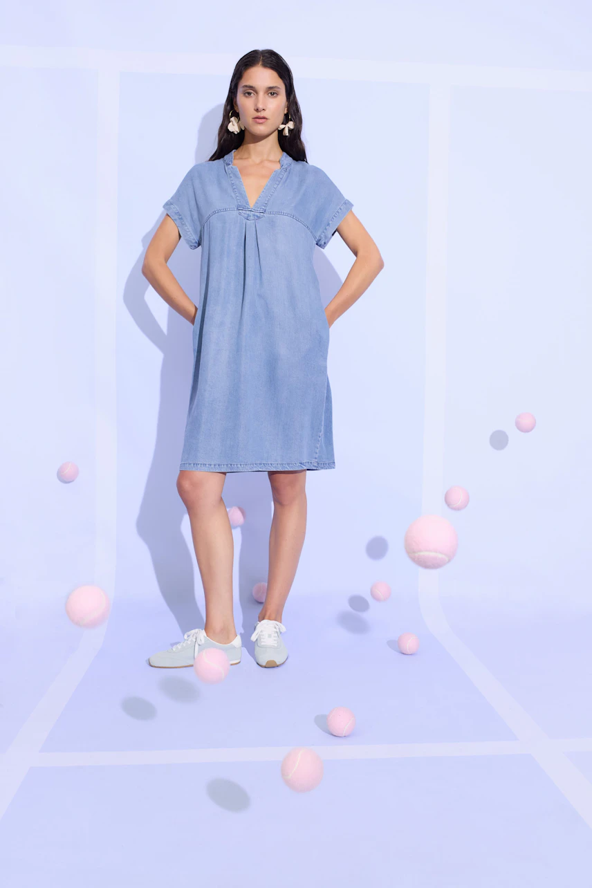 Casual denim dress: Woman in a relaxed blue jeans dress with short sleeves and white sneakers.