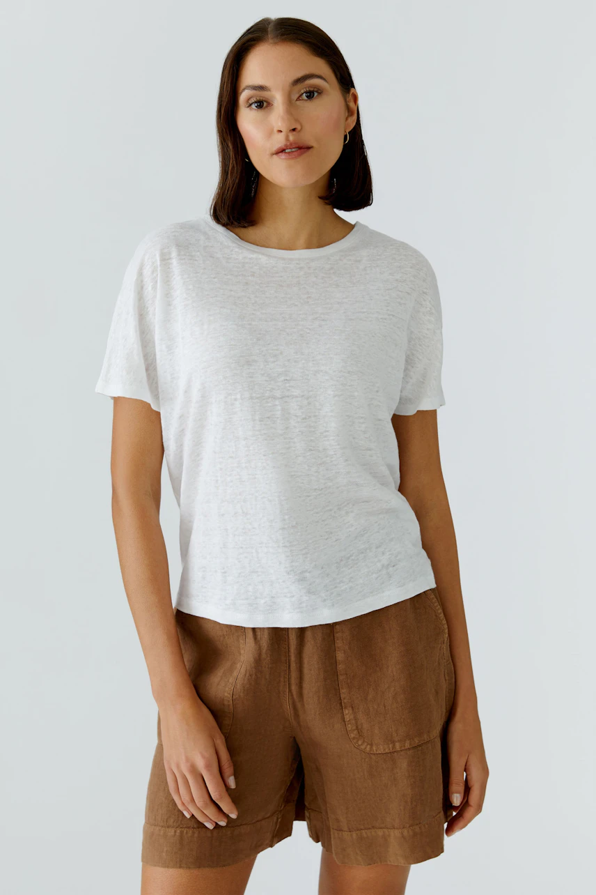 Casual women's T-shirt: Woman in a white T-shirt and brown shorts, standing confidently.