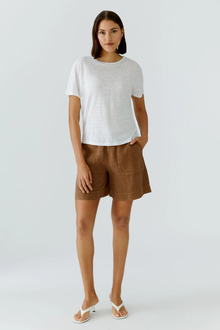 Casual women's T-shirt: Woman in a white T-shirt and brown shorts, standing confidently.