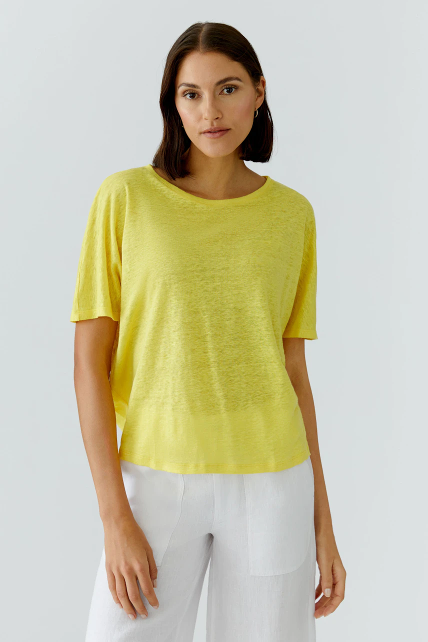 Casual women's T-shirt: Woman in a yellow T-shirt and white pants, standing confidently.