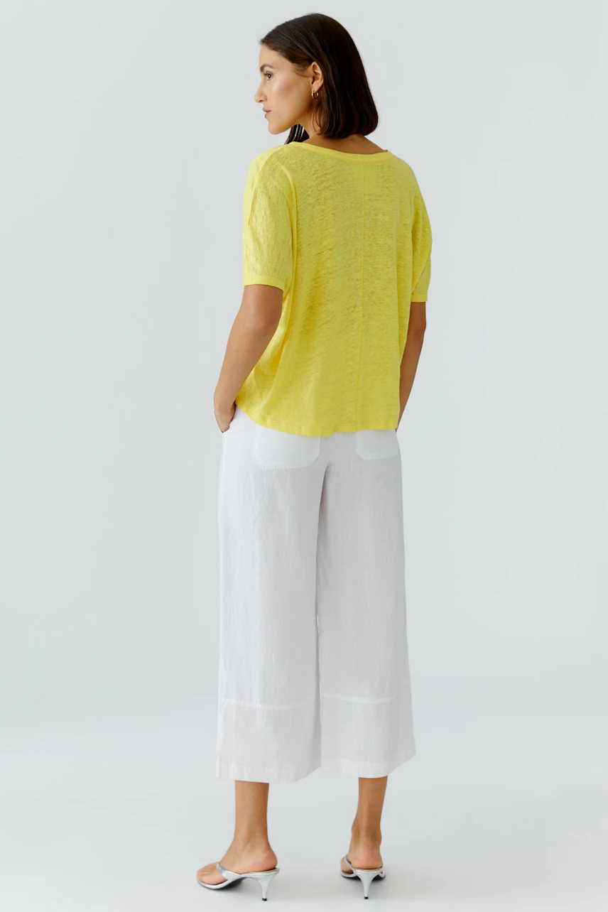 Casual women's T-shirt: Woman in a yellow T-shirt and white pants, standing confidently.