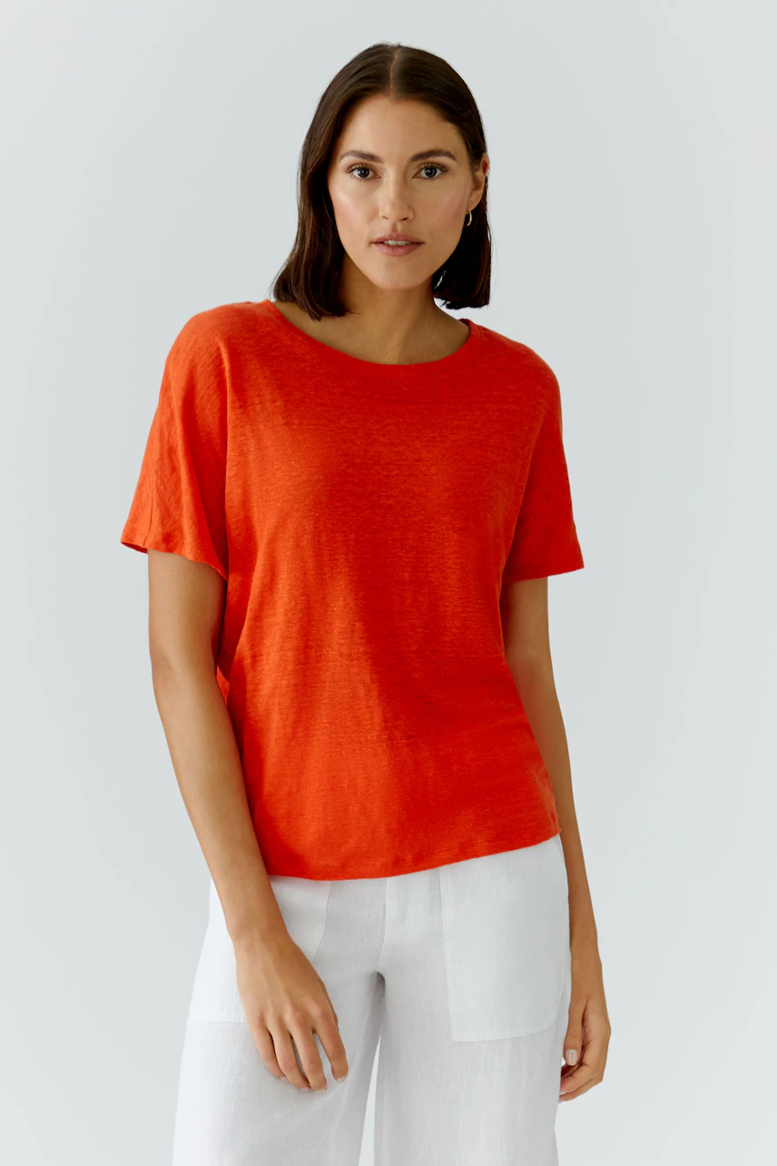 Frau im lässigen, roten T-Shirt, kombiniert mit weißen Hosen. Schlichtes Design für einen entspannten Look.