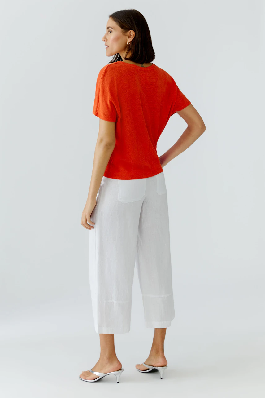 Frau im roten T-Shirt und weißen Hosen, seitlich stehend. Lässiger Look für den Alltag.