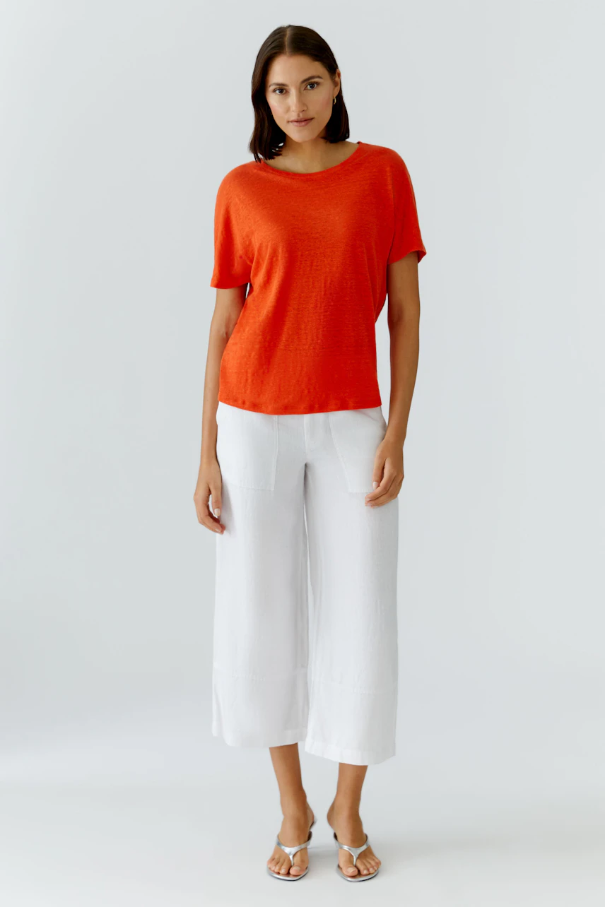 Frau im roten T-Shirt und weißen Hosen, steht selbstbewusst. Ideal für lässige Sommerlooks.